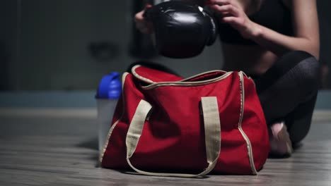 Young-beautiful-woman-sitting-on-the-floor-and-taking-from-her-bag-gloves-for-boxing,-preparing-for-training.-Shot-in-4k