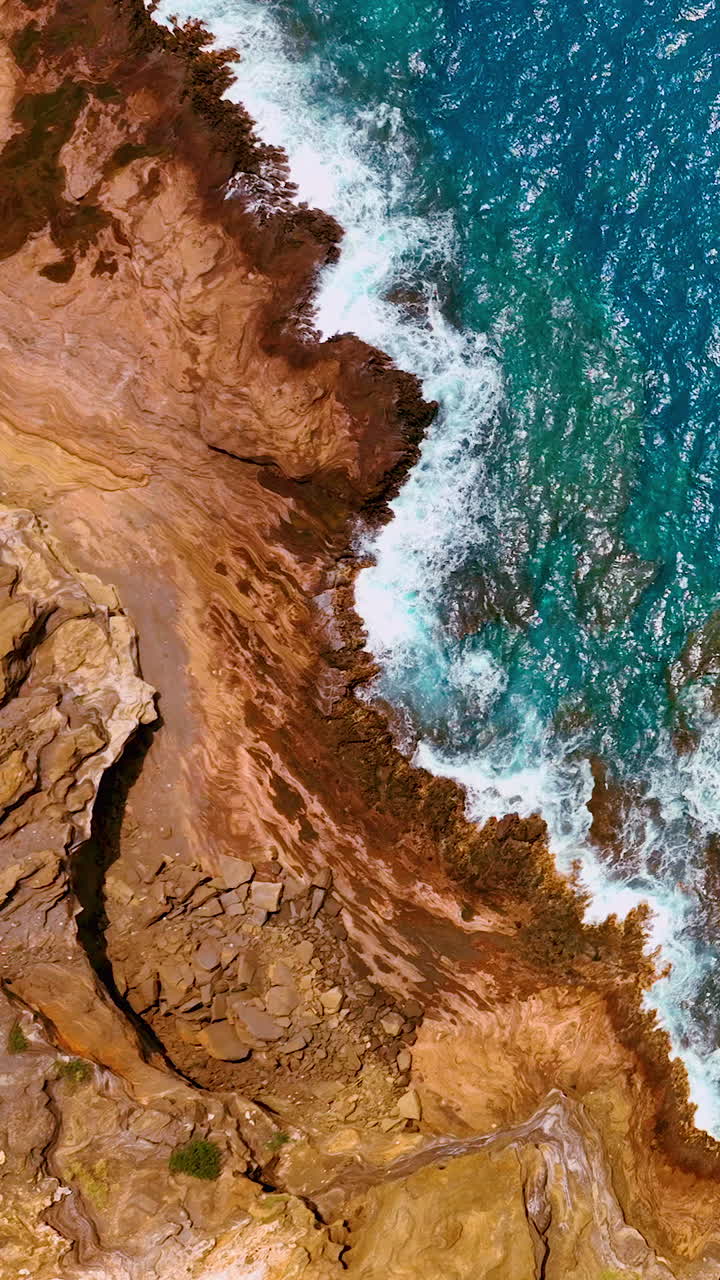 Rocce vulcaniche testurizzate che incontrano l'oceano blu con schiuma di mare bianca. Veduta dall'alto di una costa rocciosa e acqua turchese. Video verticale.