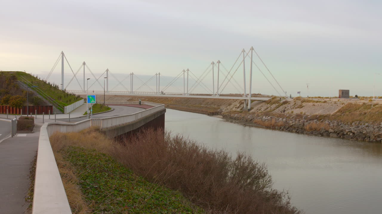 Motion video of a river passing under "La passerelle du Grand Large" bridge in the background in Dunkirk, France during daytime.