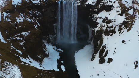 Aerial-view-tilting-over-the-Skogafoss-waterfall,-cloudy-winter-day-in-Iceland