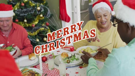 Animation-of-merry-christmas-text-in-red-over-happy-diverse-senior-friends-at-christmas-dinner-table