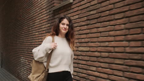 Young-girl-smiling-at-the-camera-while-walking-by-brick-wall-in-the-street