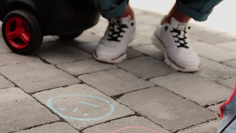 a father and his child draw with chalk on the ground in front of the home