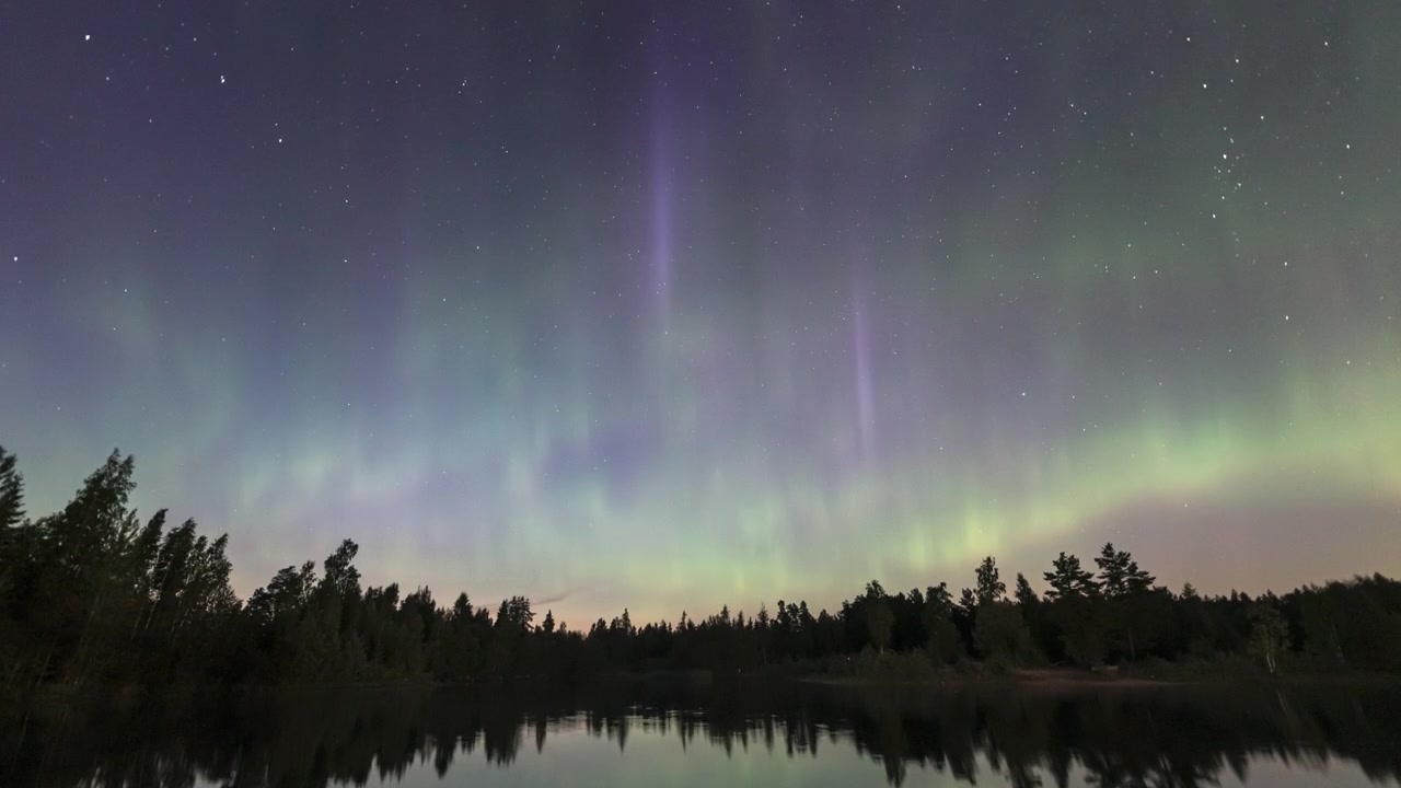 Time Lapse dell'Aurora Boreale che si riflette su un lago calmo con foresta