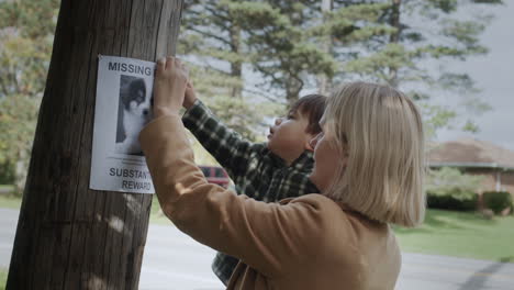 a mother and a young boy attach an announcement about a missing puppy together. search and disappearance of pets