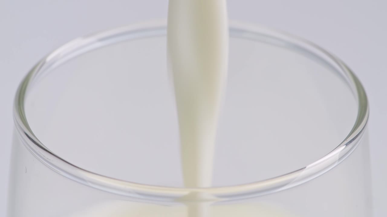 close up de leche que se vierte en un vaso de beber sobre un fondo blanco