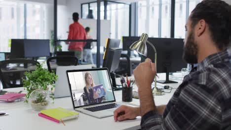 Mixed-race-businessman-sitting-at-desk-using-laptop-having-video-call-with-female-colleague