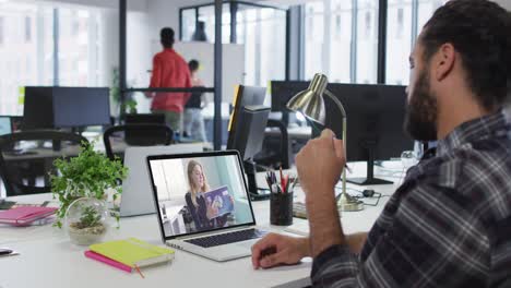 hombre de negocios de raza mixta sentado en un escritorio usando una computadora portátil haciendo una videollamada con una colega