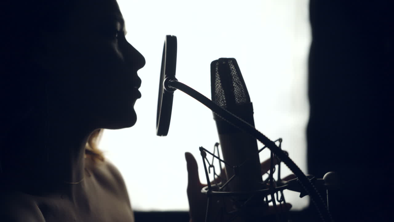 Silhouette of beautiful woman is singing a song in front of a microphone in an audio recording studio on a white background. Close-up