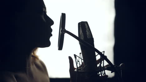silhouette of beautiful woman is singing a song in front of a microphone in an audio recording studio on a white background. close-up