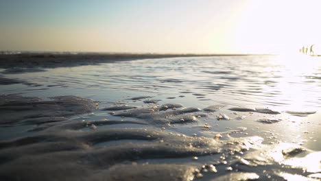 foto macro de espuma en la arena con un paisaje marino tranquilo en el fondo al amanecer