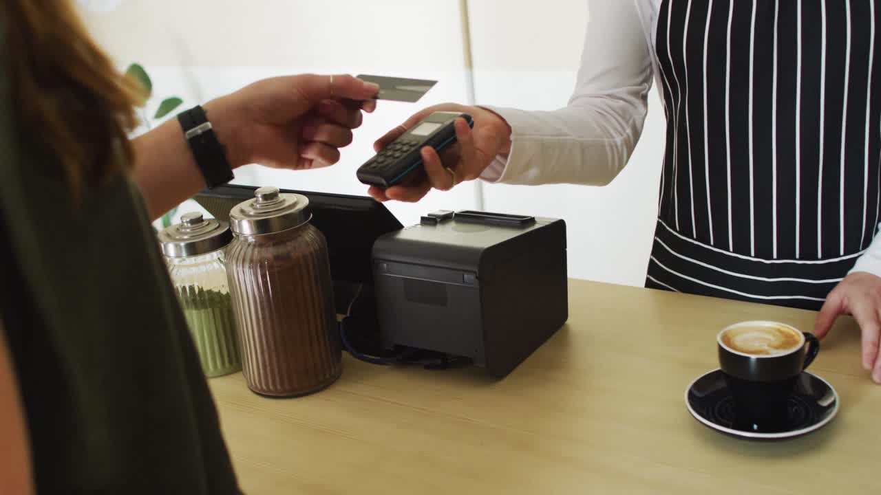 Cameriera caucasica che riceve un pagamento contactless e consegna una tazza di caffè a una cliente caucasica.