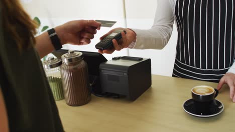 camarera caucásica recibiendo un pago sin contacto y dando una taza de café a una cliente caucásica