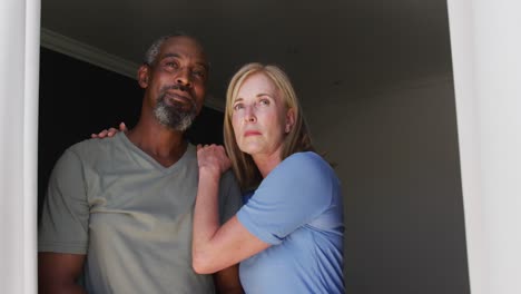 pareja de alto nivel de raza mixta abrazándose mientras miran por la ventana en casa