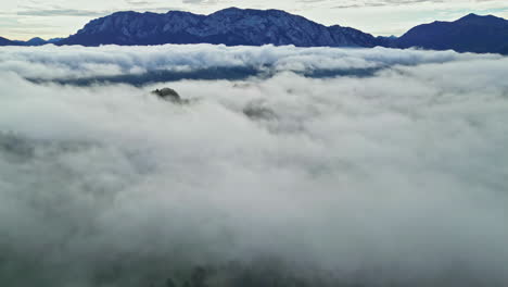 aerial shot of hilly landscape covered by thick layer of clouds with visible snowcapped mountain in the background