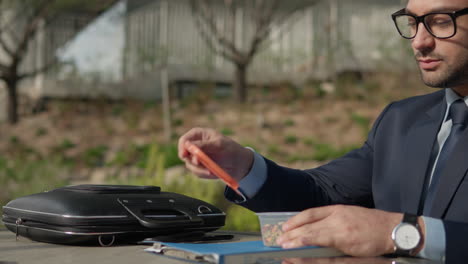 office worker having lunch outside - business man takes plastic lunchbox with nuts out of suitcase, opens it, and enjoys eating organic almonds and walnuts sitting in a park - tracking slow motion