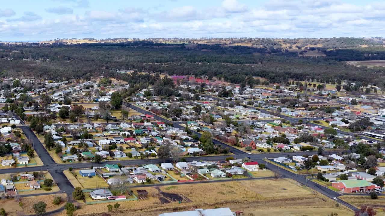 Drone footage glides over Coonabarabran, New South Wales, revealing residential neighborhoods, sports fields, and surrounding countryside under bright daylight with steady camera movement