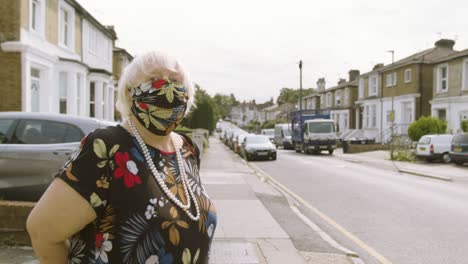 elderly woman wearing a face mask with matching dress walking onto the street waving and walking past camera