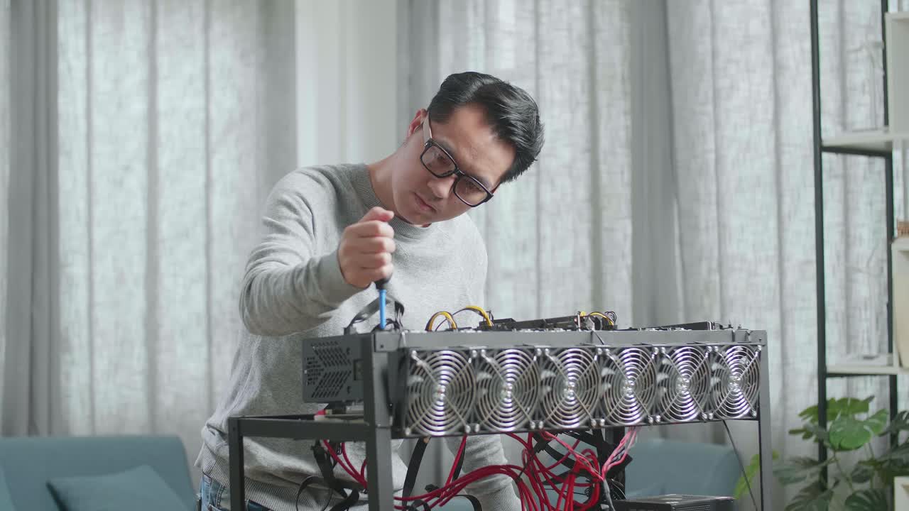 안경을 쓴 아시아인 남자가 암호화폐를 채굴하기 위해 채굴 기계를 청소합니다.