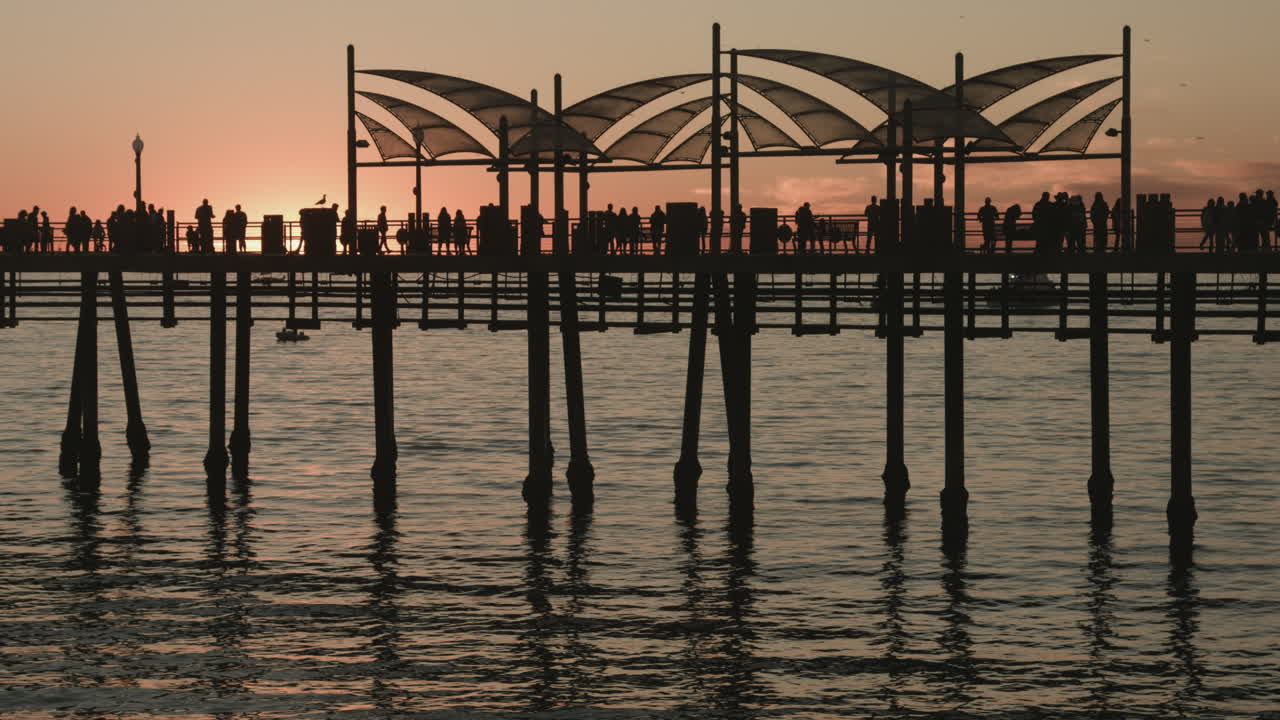 Metraje cinematográfico UHD del muelle de Redondo Beach al atardecer, mostrando olas del océano, pescadores, visitantes paseando, un cielo vibrante y el pintoresco estilo de vida costero del sur de California.