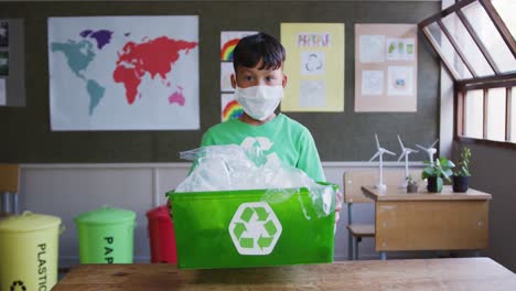 boy wearing face mask holding recycle container in class at school