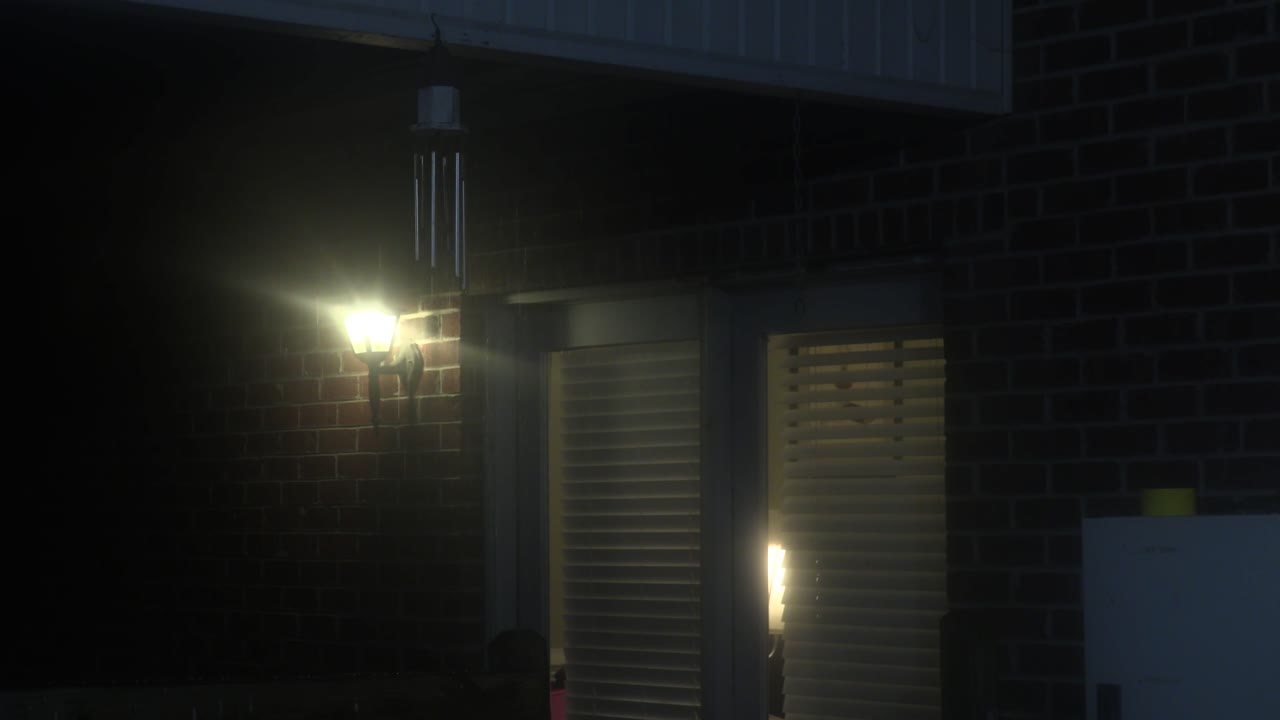 Night scene of a brick house with a lit doorway and wind chimes