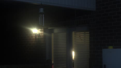 night scene of a brick house with a lit doorway and wind chimes