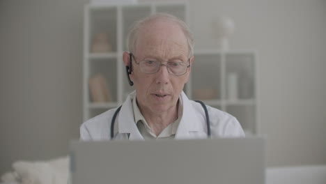 elderly professor of medicine is using laptop for online consulting of patients and intern students from his office