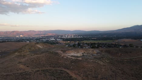 Toma-Aérea-Que-Revela-El-Horizonte-De-Reno,-Nevada-Desde-Detrás-De-Una-Colina-En-El-Desierto-Cercano