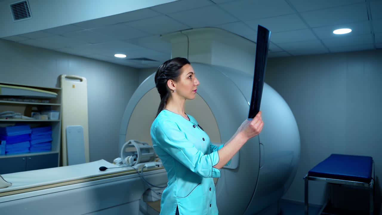 Female radiologist with x-ray photo. Side view of a medical worker examining x-ray picture while standing near the MRI machine in hospital.