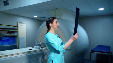 female radiologist with x-ray photo. side view of a medical worker examining x-ray picture while standing near the mri machine in hospital.