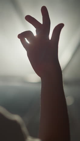 child plays with finger in room at backlight. little girl has fun with light and shadow in hotel closeup. curious kid palm against glowing lamp