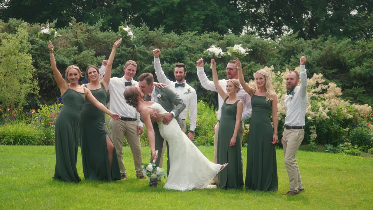 Bride and groom kiss while bridal party cheers and lifts arms in celebration in a garden setting