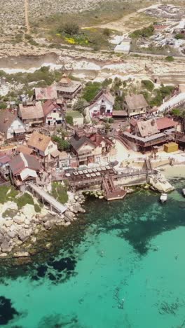 aerial view of popeye village by clear turquoise waters in malta vertical