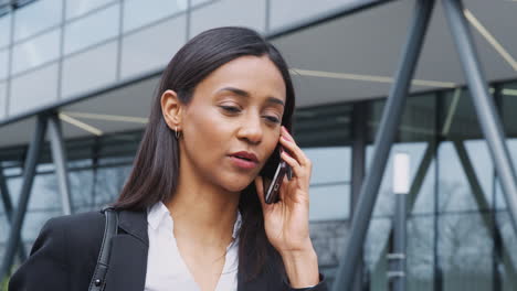 businesswoman commuting to work talking on mobile phone outside modern office building