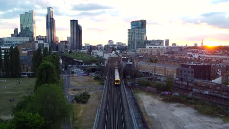 cinematic drone shot train travelling on railway in city at sunset