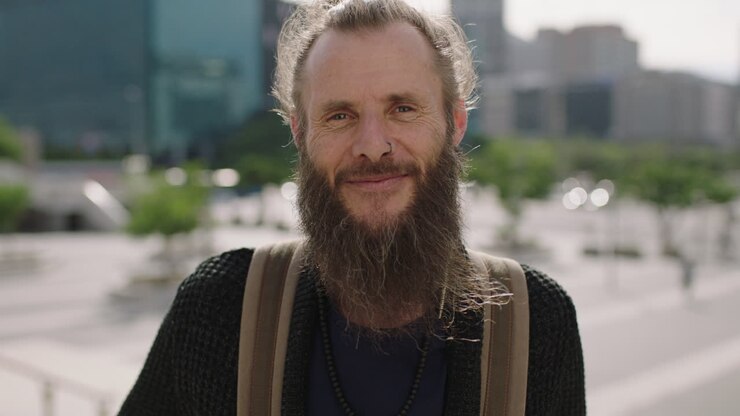 ritratto ravvicinato di un uomo hippie maturo allegro che sorride felice in una città urbana soleggiata godendo dello stile di vita di viaggio