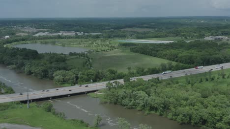 drone flies towards a midwestern highway in the usa as it crosses over a muddy river in the summer