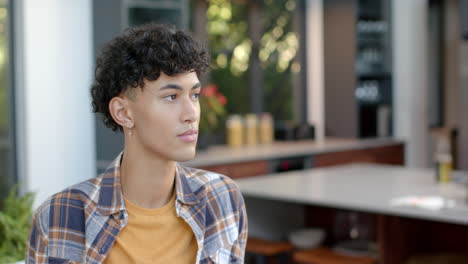 sitting in modern kitchen, young man with curly hair looking thoughtful, copy space