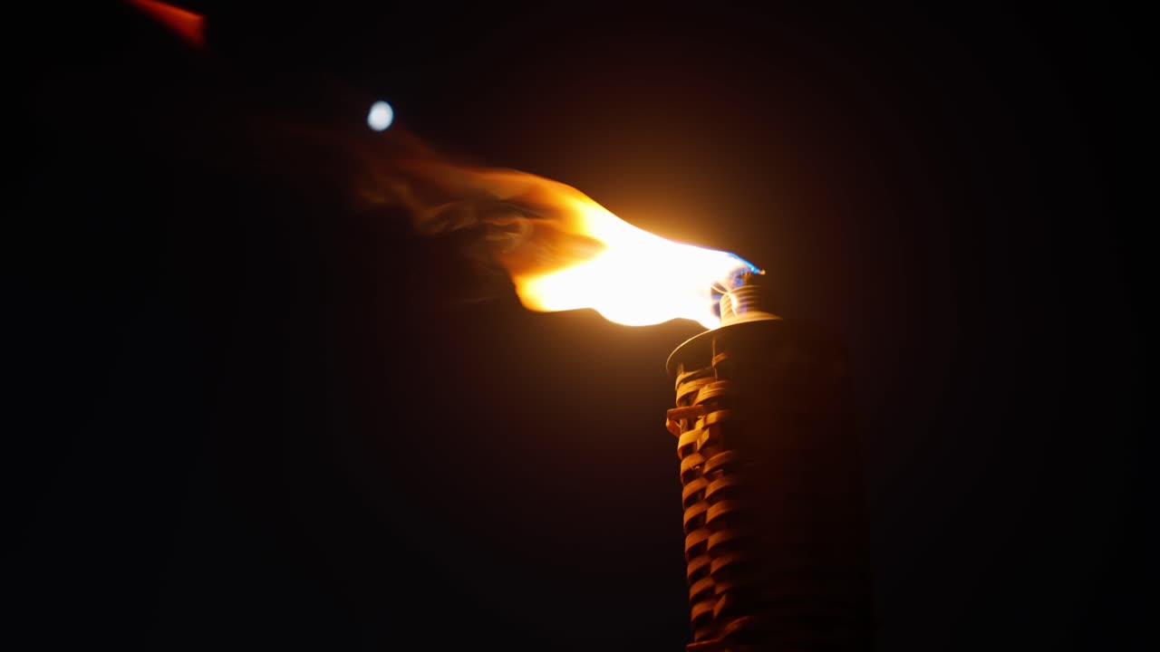 Close up shot of bamboo torch burning at night with moon in the background. Flame flickering in gust of wind
