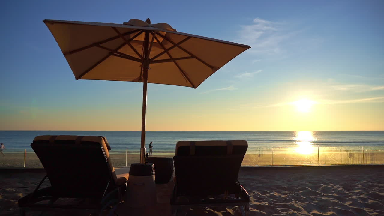 Due sedie a sdraio sotto un ombrellone su una spiaggia tropicale al tramonto. Mare della costa deserto al tramonto