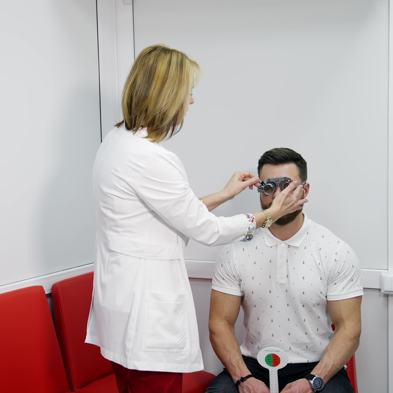 Eyesight test in clinic. Female optician in lab coat adjusting lens in trial frame of a patient. Doctor covers another eye with a lens in testing glasses. Slow motion