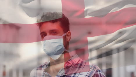 animation of flag of england waving over man wearing face mask during covid 19 pandemic