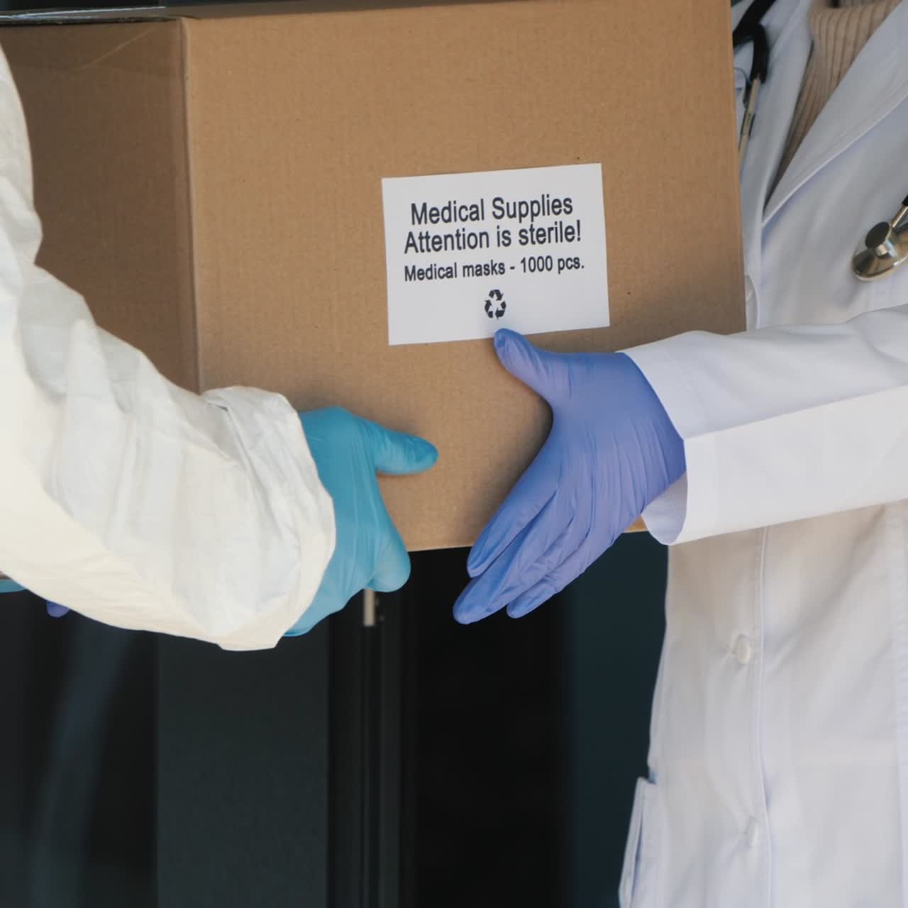 A una persona con un traje protector se le entrega una caja con mascarillas médicas protectoras para el médico