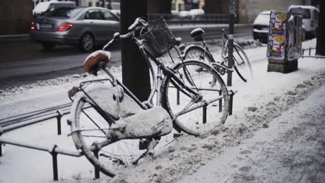 pair of bikes covered with snow left on street tied to poles by side of road