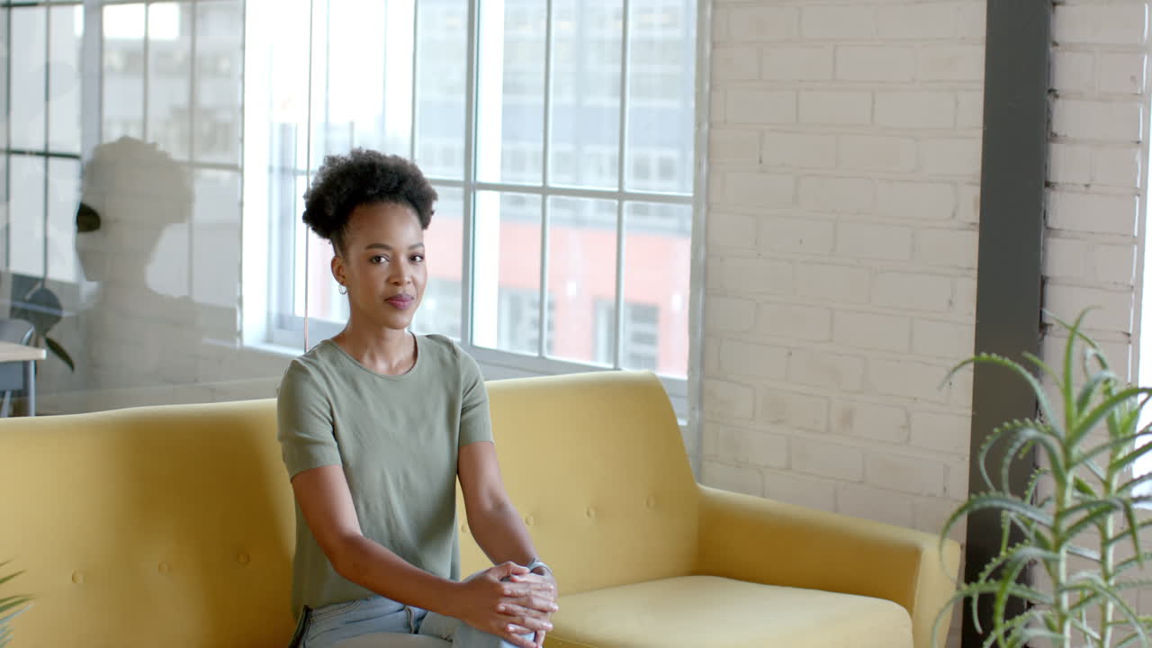 Una giovane donna afroamericana è seduta su un divano giallo in un ambiente d'ufficio con spazio per il testo.