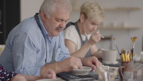 a group of elderly people at a master class in pottery together sculpt and cut a drawing on cups of clay for the manufacture of ceramic dishes