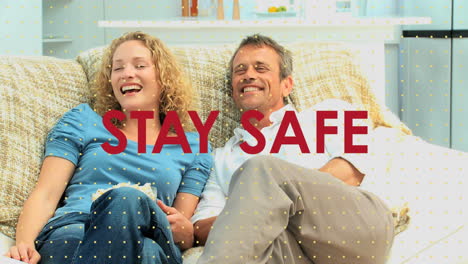 animation of social distancing message over caucasian couple lying on couch