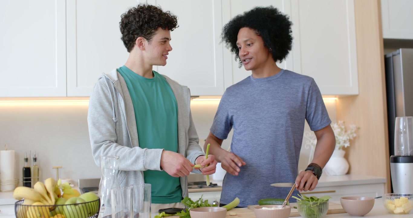 Diverse male friends starting salad prep for lunch, peeling celery and slicing greens on board