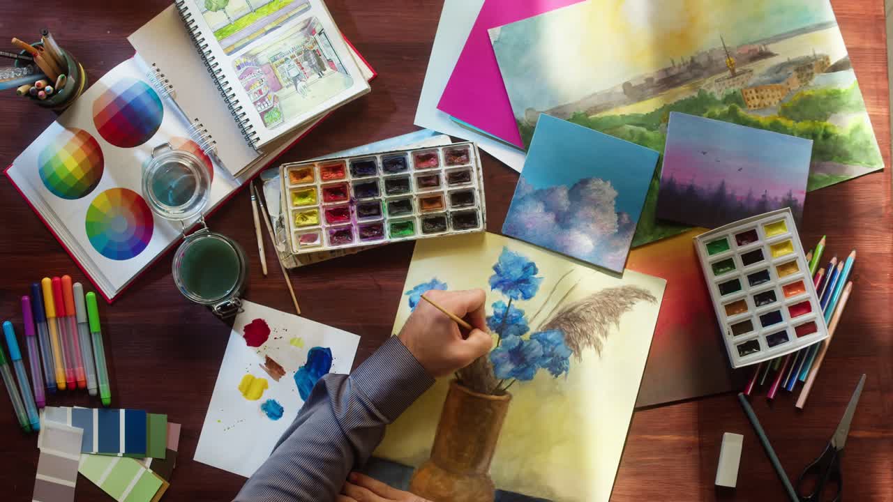 Artista pintando flores de acuarela en un escritorio con materiales de arte